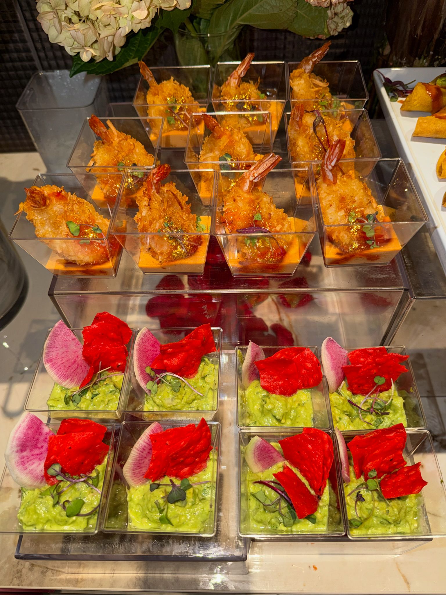 Buffet con rolls de sushi, vasitos de guacamole y decoración floral